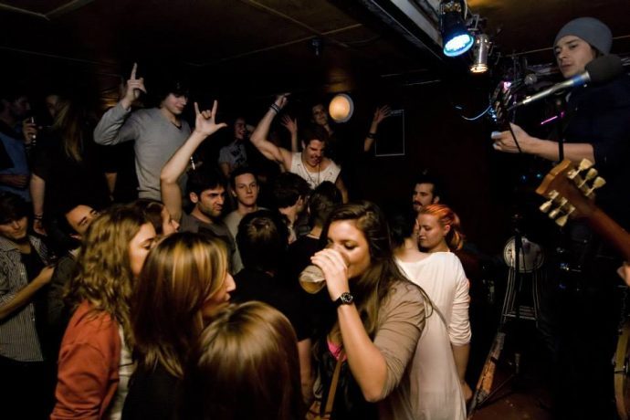 Menschen tanzen und trinken in einem dunklen Nachtclub, in dem eine Band spielt