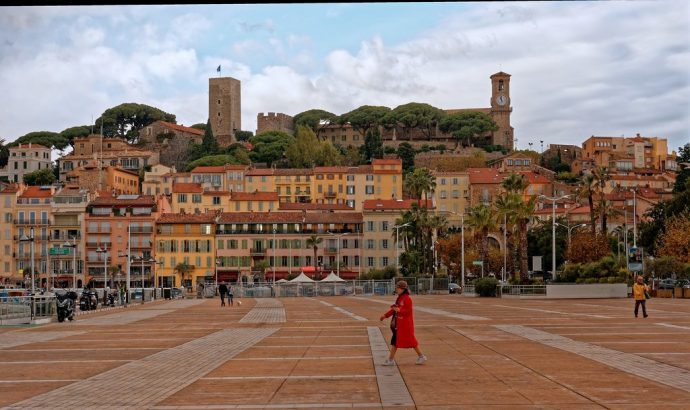A woman in red walking across a plaza in front of old historic buildings of Cannes