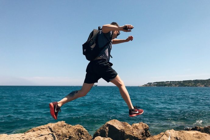 En man i sportkläder och ryggsäck springer längs den klippiga kusten
