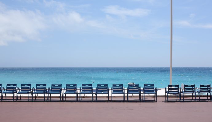 Blå stolar med utsikt över det azurblå havet en solig dag på Promenade des Anglais